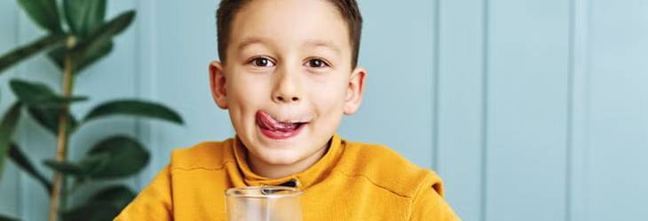 Niño tomando un vaso de leche, alimento que contiene calcio