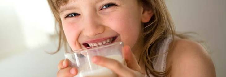 Niña sonriendo mientras toma un vaso de leche con calcio