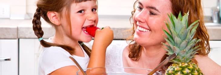 Mamá le da a su hija una ensalada de frutas en la cocina