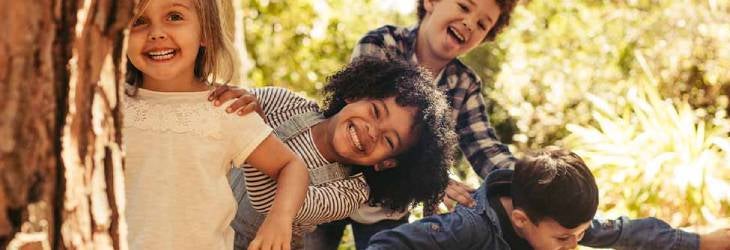 Niños se esconden tras un árbol y se divierten haciendo actividades recreativas