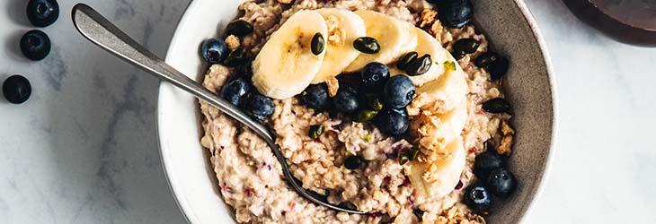 Servido a la mesa desayuno compuesto por bayas, plátano y avena, fuente de fibra